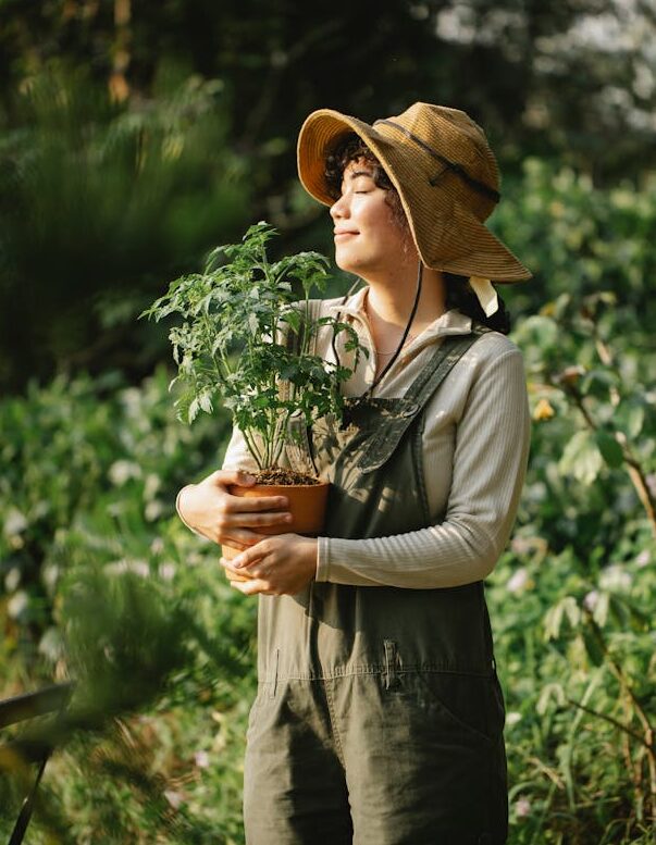 A smiling young female adult holding  a thriving potted plant. She is a happy and confident gardener!