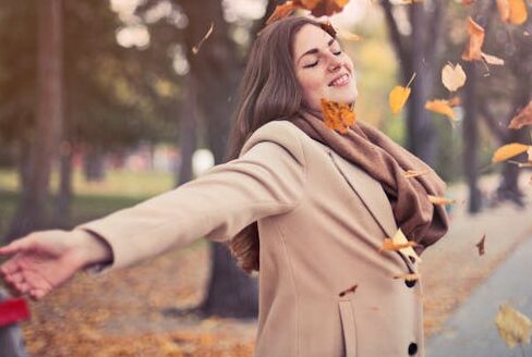 A lady walking outside. Throwing leaves in the air feeling calm, happy andenergized