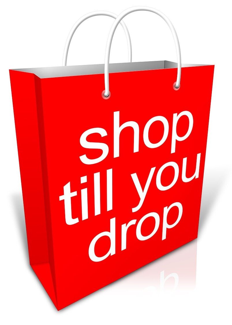 The image features a cartoon shopping bag in bright red, with white handles. On the front of the bag, the phrase 'Shop Till You Drop' is written in bold white letters. The lack of a background emphasizes the bag, symbolizing the overwhelming consumerism that often overshadows the true spirit of the holiday season.