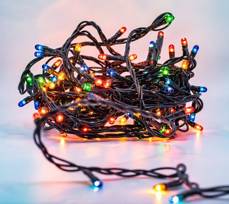 The image shows a tangled pile of mini tree lights scattered on a shiny floor. The lights are illuminated, creating a vibrant glow amidst the chaos. The tangled cords and bulbs emphasize the frustration often encountered while decorating for the holidays, capturing the essence of decorating disasters.